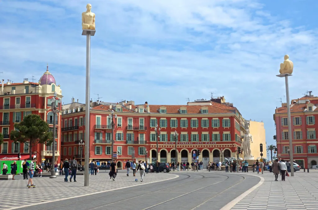 Place ensoleillée avec statues et bâtiments colorés.